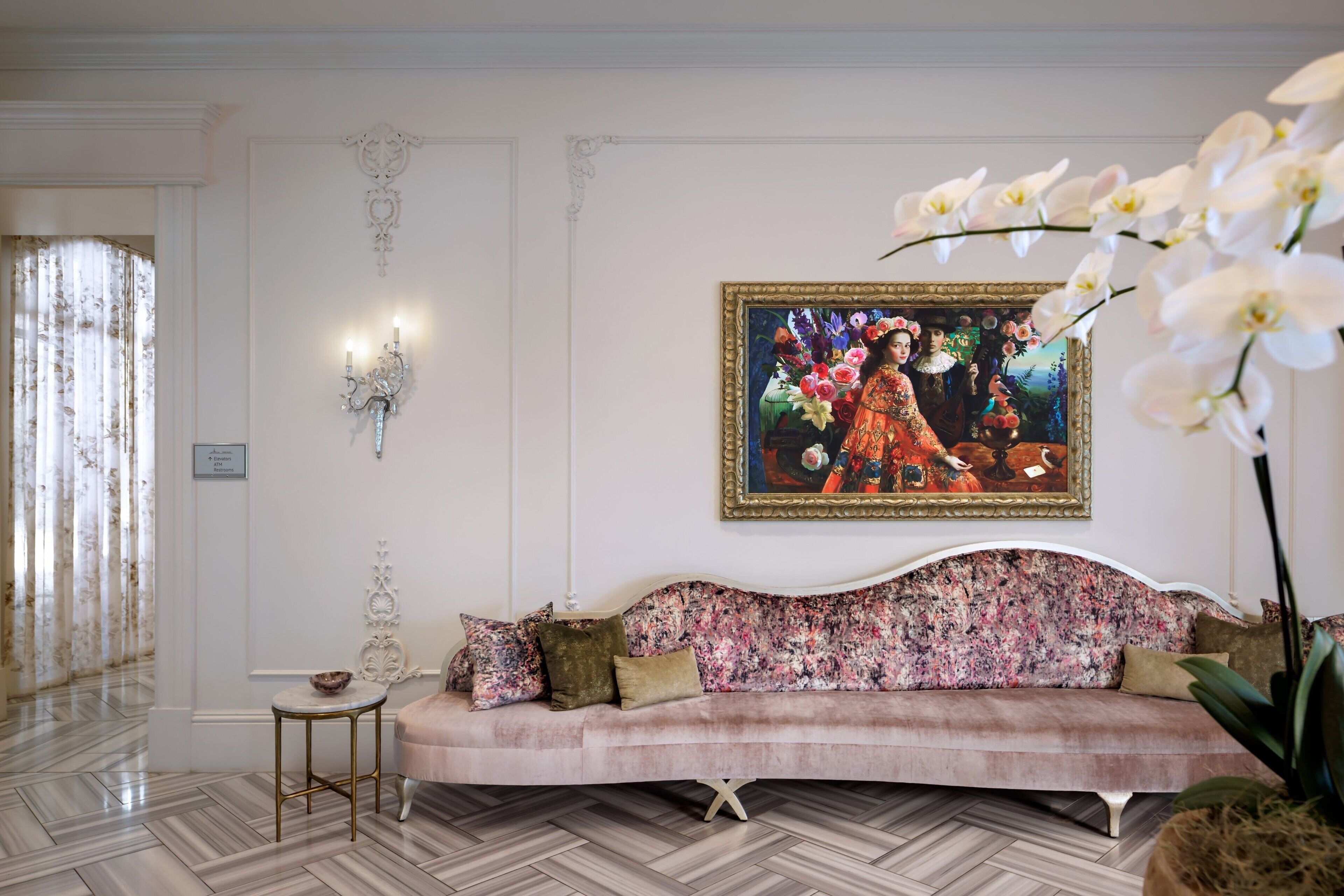 A room with a floral sofa, a painting on the wall, and a potted plant.