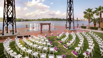 Montaje de una ceremonia de boda al aire libre con sillas blancas dispuestas en semicírculo, un arco floral y vistas a un cuerpo de agua.