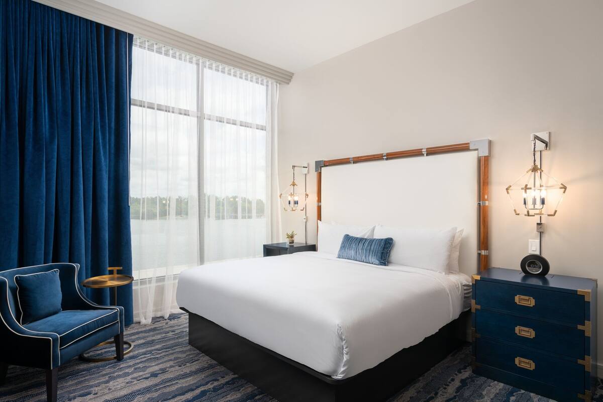 A hotel room with a large bed, a chair, a bedside table, and a dresser.