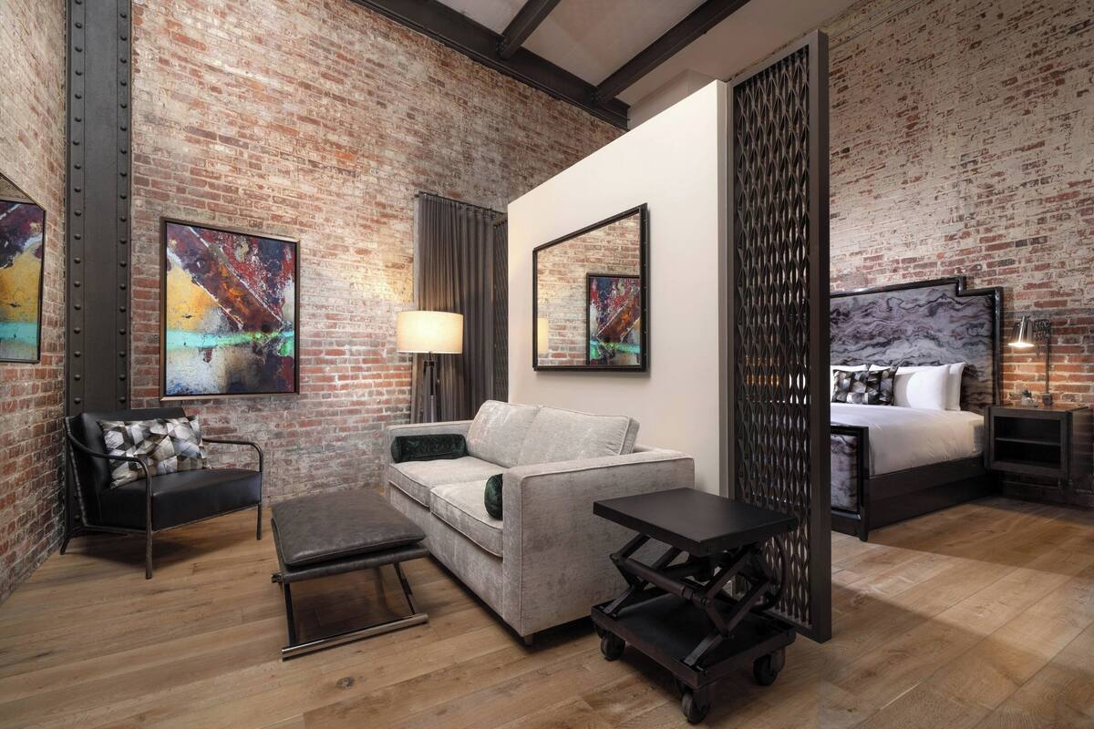 A room with a brick wall, a sofa, a chair, a bed, and artwork.