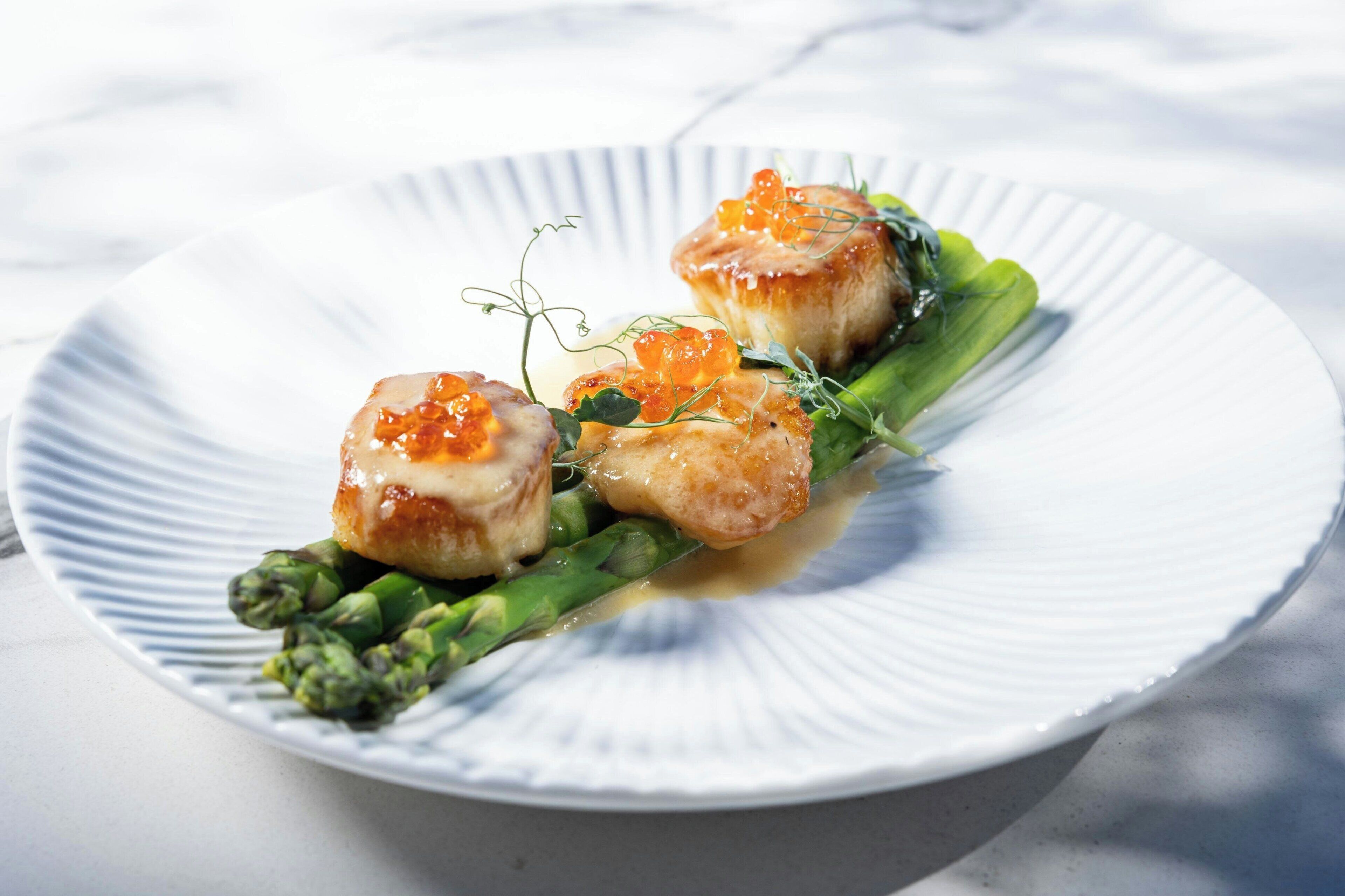 A plate with seared scallops, caviar, and asparagus.