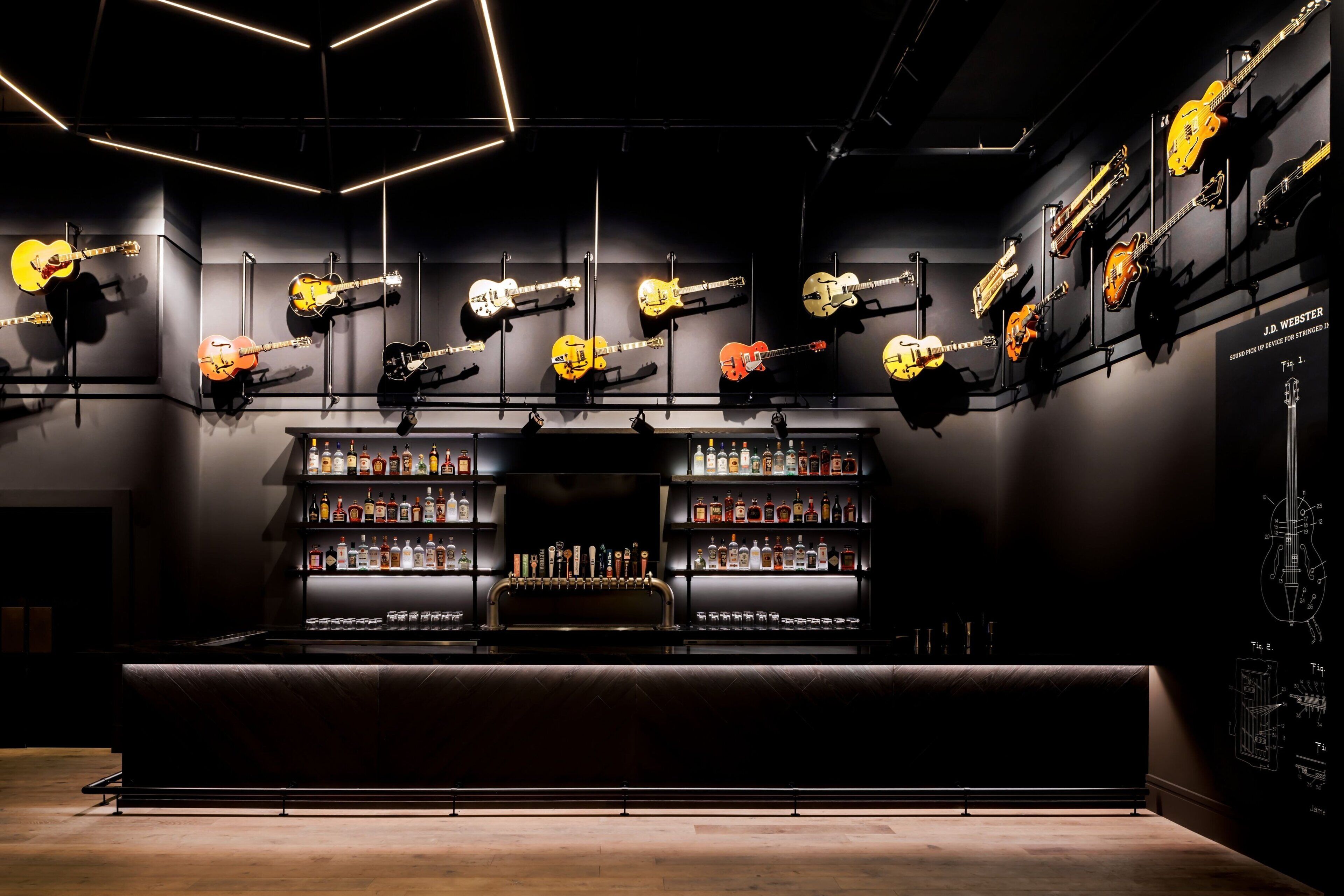 A bar area with multiple guitars displayed on the wall and a well-stocked liquor shelf.