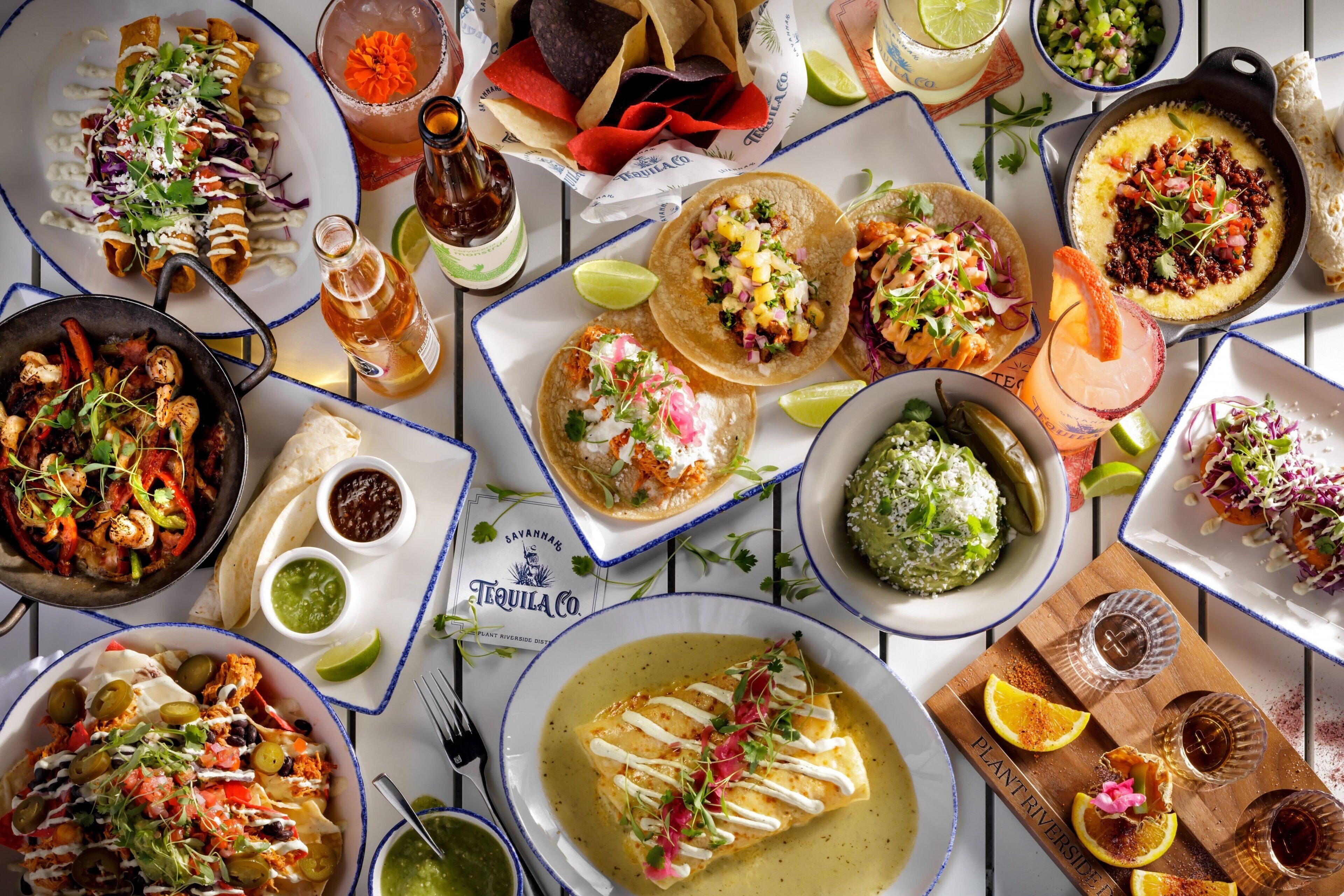Une variété de plats, notamment des tacos, des enchiladas et un bol de soupe, disposés sur une table avec des boissons et des condiments.