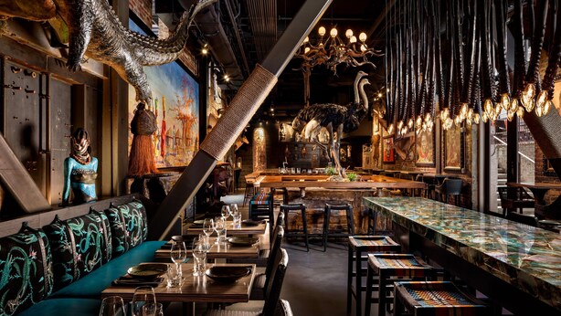 A restaurant with a long communal table, booths, and a high ceiling with hanging lights. - JW Marriott Savannah Plant Riverside District (Savannah)