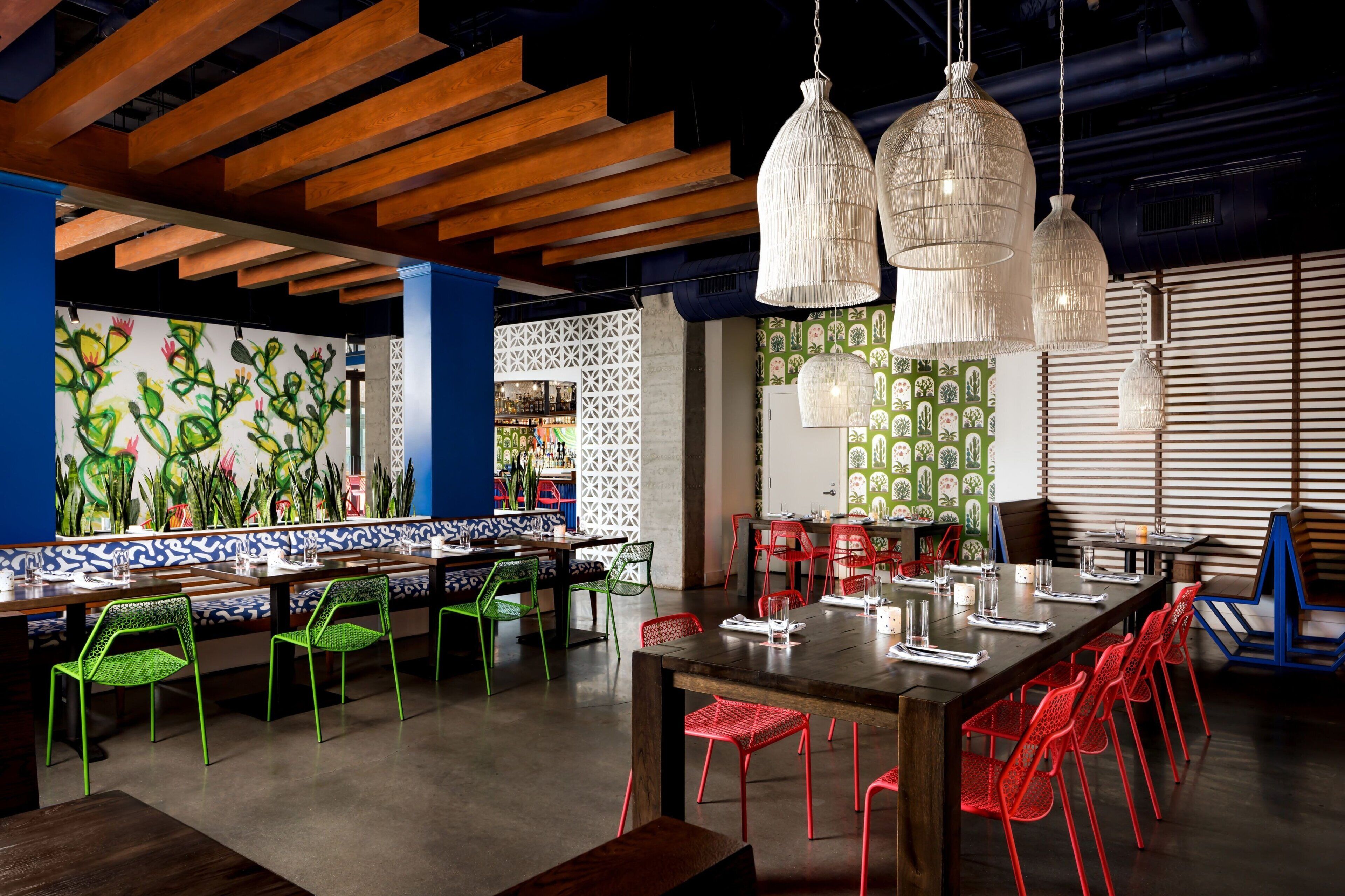 Un restaurant avec des poutres en bois au plafond, des chaises vertes et rouges, et des lampes suspendues blanches.