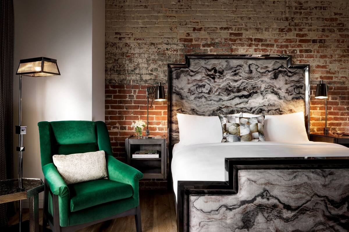 A modern hotel room with a brick wall, a green armchair, a marble-patterned bed, and two bedside lamps.