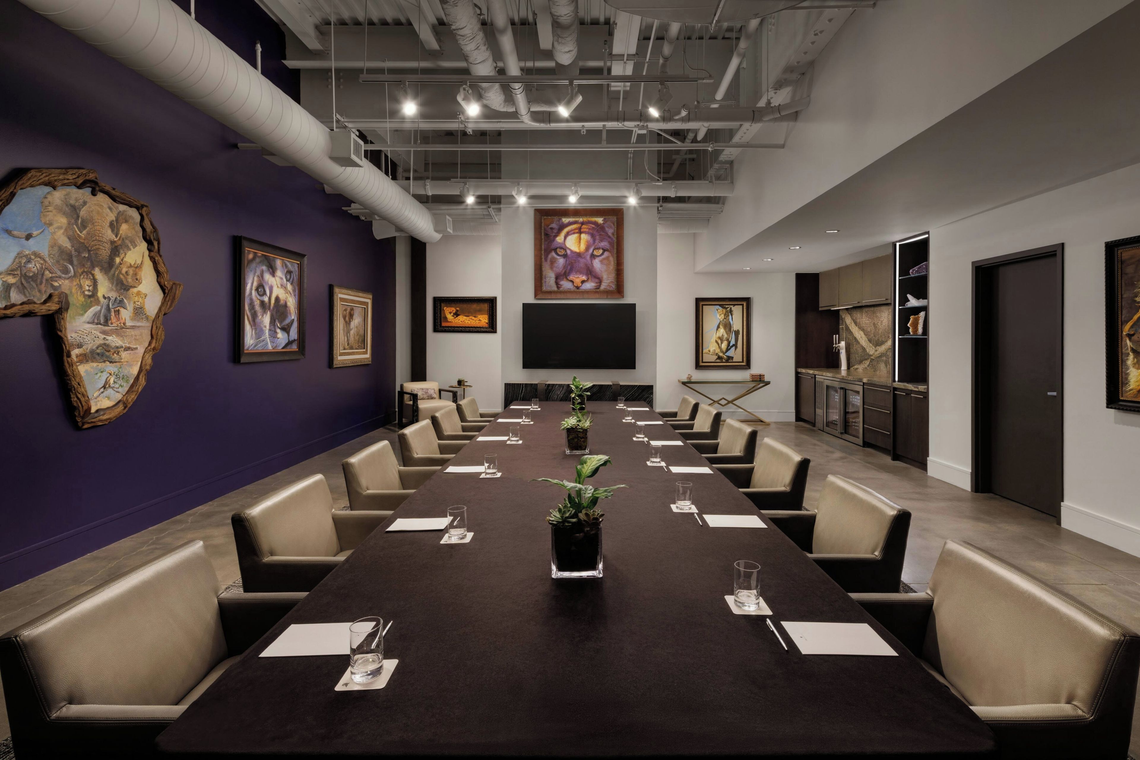 A conference room with a long table, chairs, and a large screen.