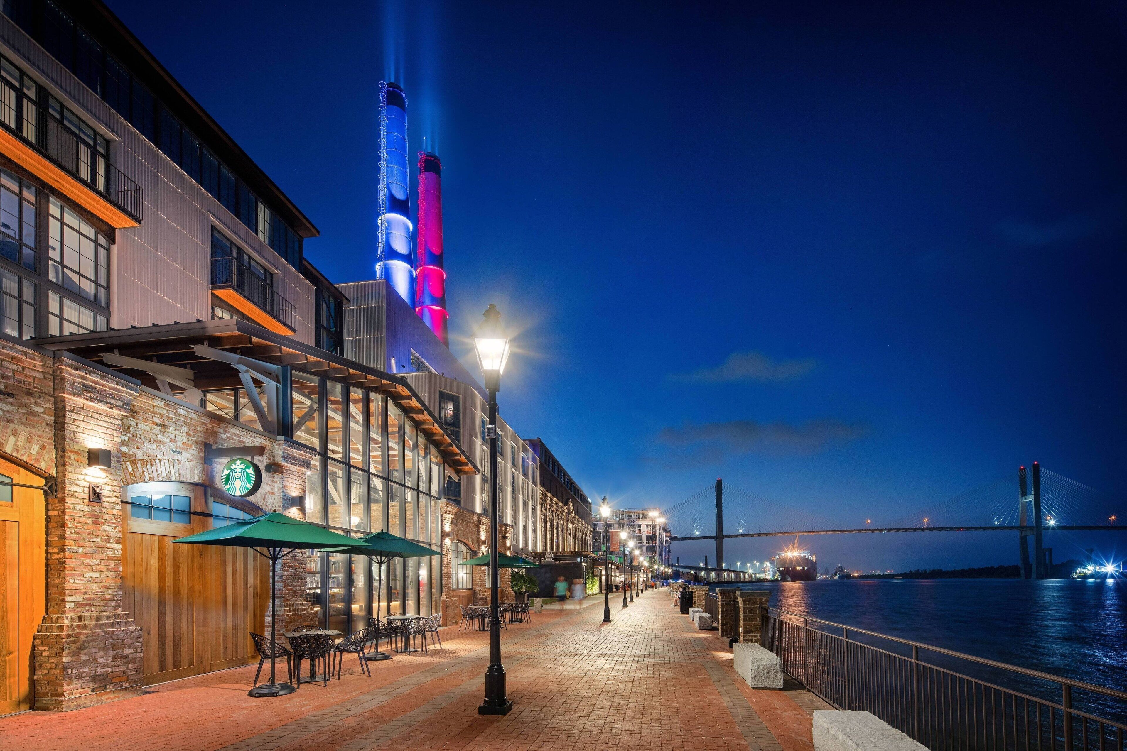 A waterfront restaurant with outdoor seating, a view of the river, and a bridge in the background.