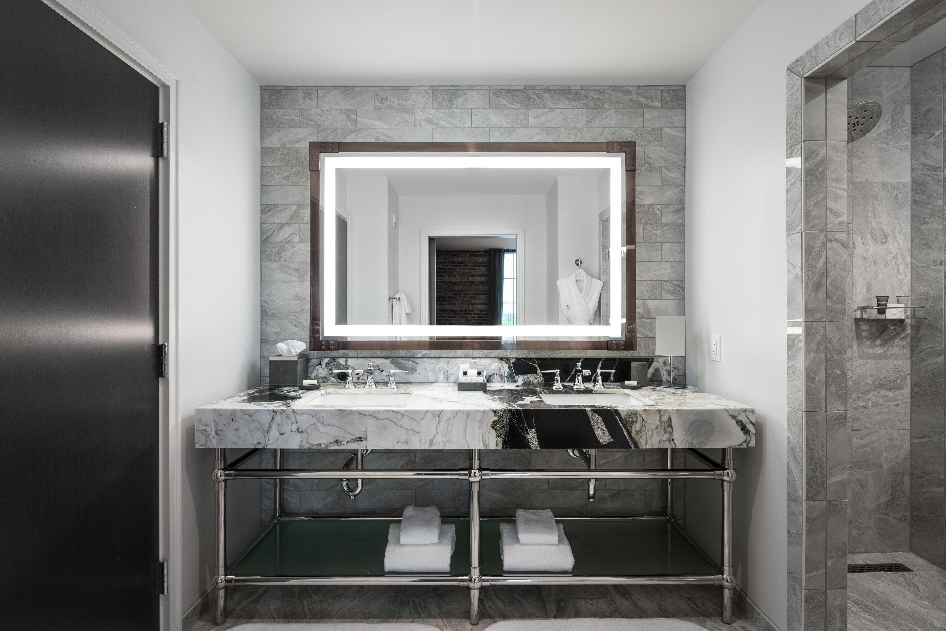 A modern bathroom with a large mirror, dual sinks, and a walk-in shower.