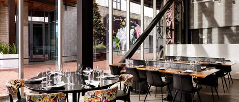 An outdoor dining area with round tables and chairs, a staircase, and a mural on the wall.