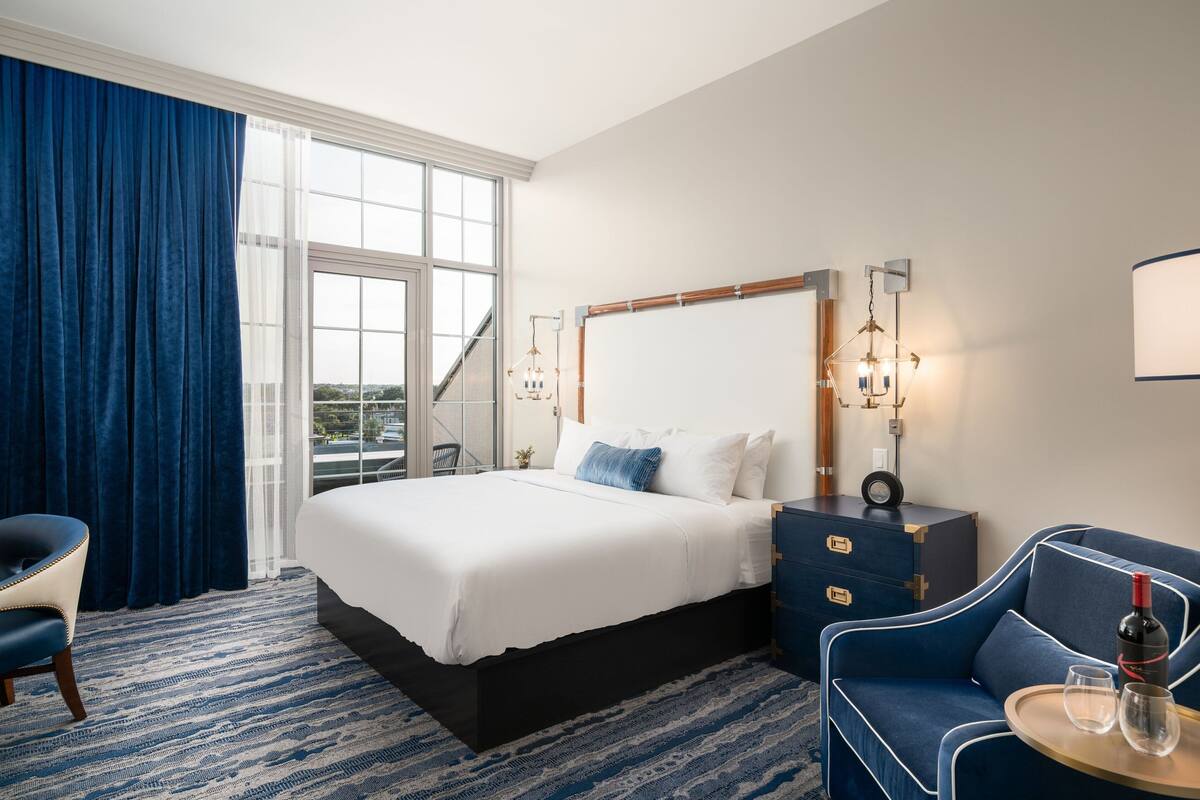 A hotel room with a large bed, a desk, a chair, and a view of the outdoors.