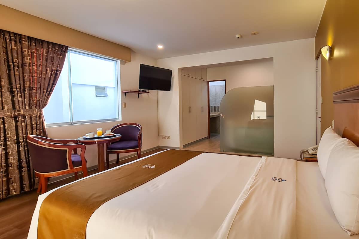 A hotel room with a large bed, a desk with a chair, a TV mounted on the wall, and a bathroom visible through an open door.