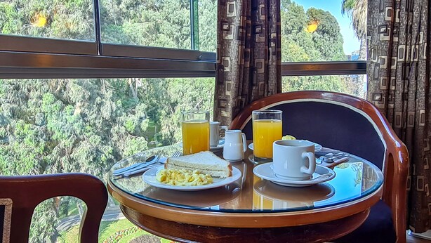 A dining table with breakfast items, a view of a forest through large windows, and patterned curtains. - 44 Vip Hotel (Lima)