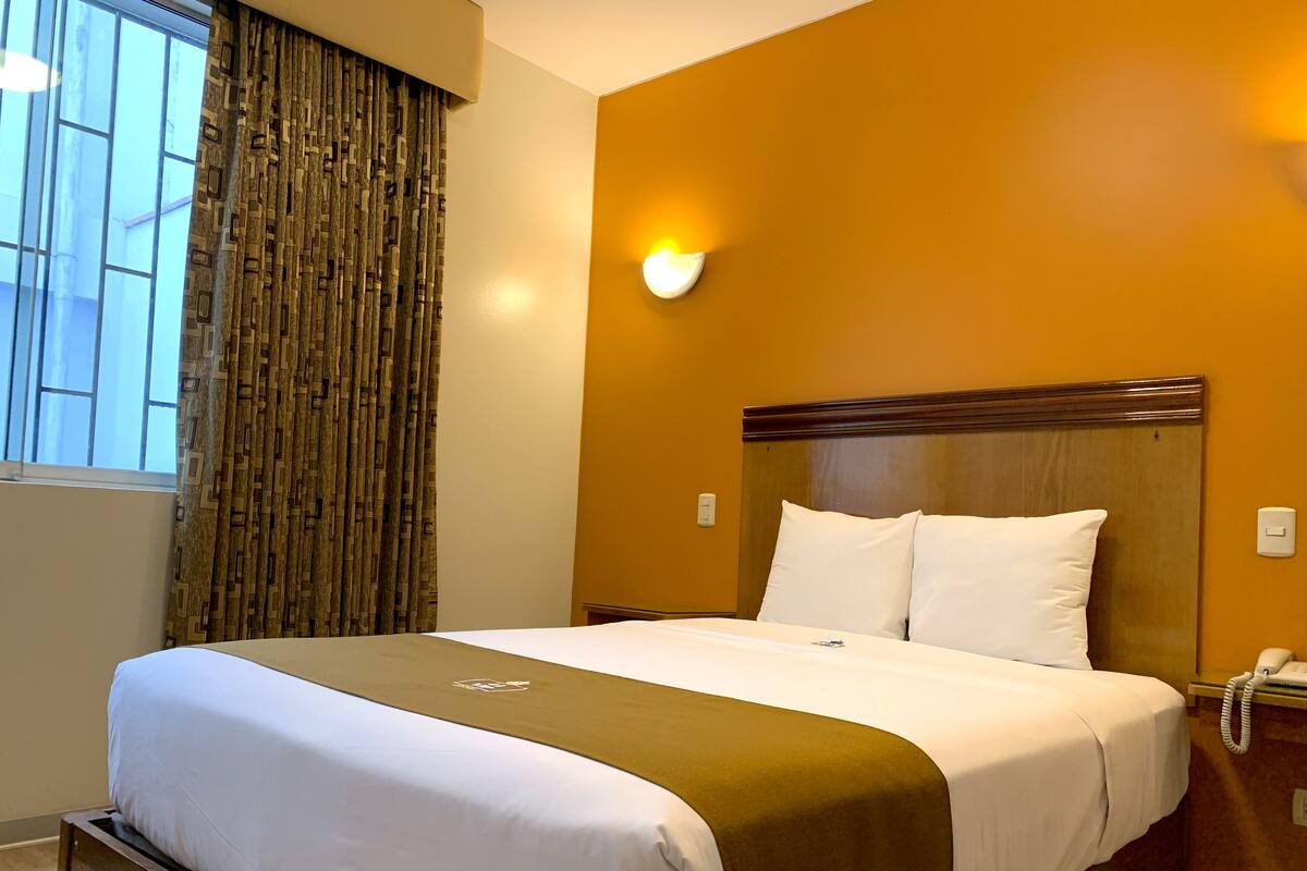 A hotel room with a bed, a telephone, and a wall-mounted light.