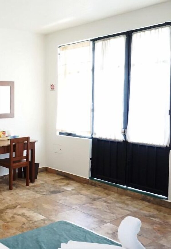 Una habitación con escritorio, silla y un ventanal con cortinas.