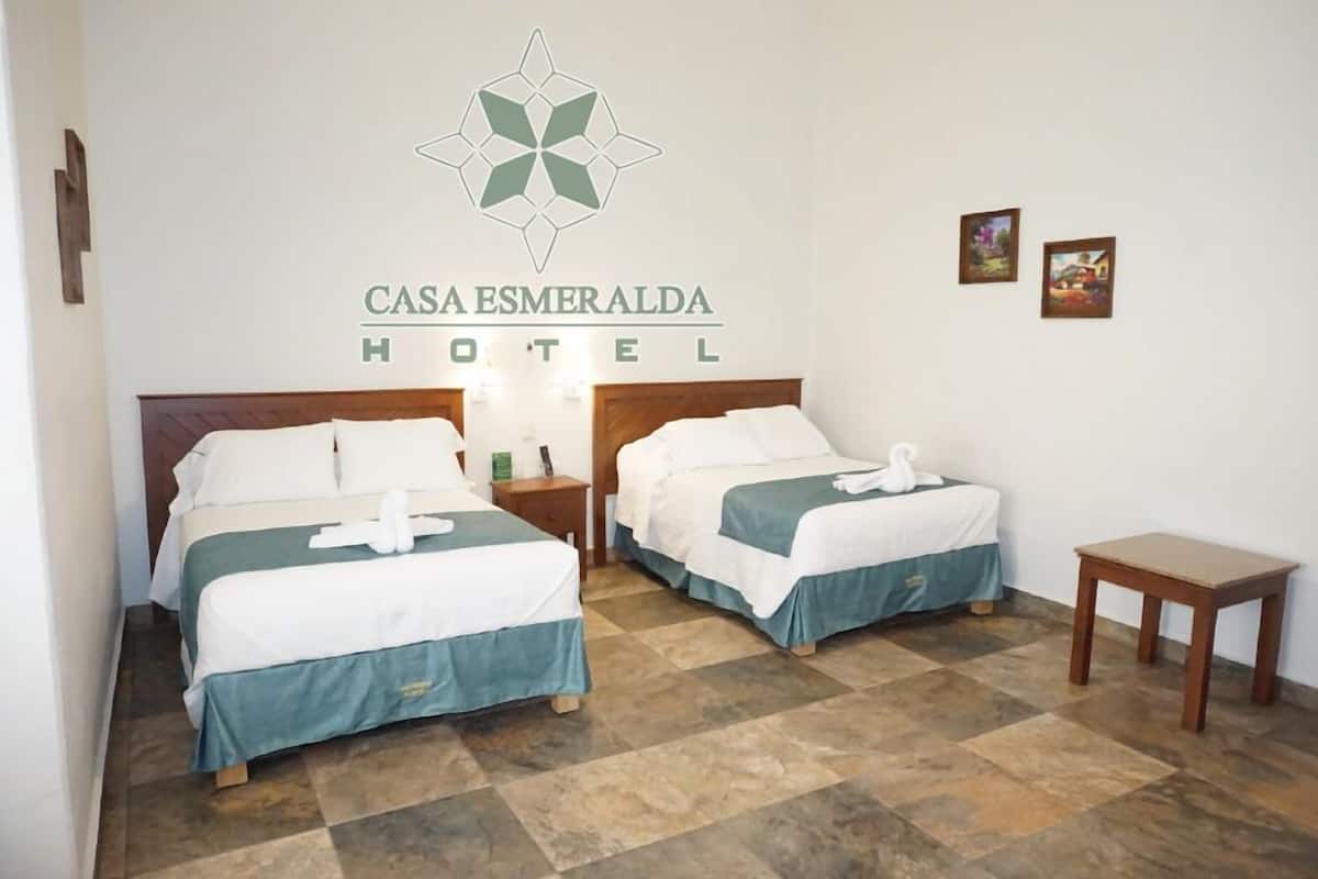 A hotel room with two beds, a small table, and a wall-mounted logo.