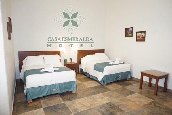 A hotel room with two beds, a small table, and a wall-mounted logo. - Casa Esmeralda Hotel (Oaxaca)