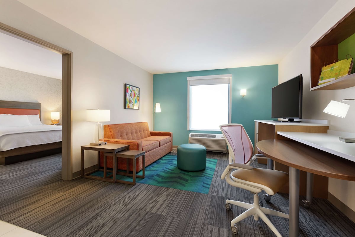 Habitación de hotel con cama, sofá, escritorio, silla, televisor y ventana.