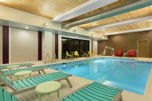 Piscina interna com espreguiçadeiras e mesas, teto de madeira e chão revestido de azulejos.