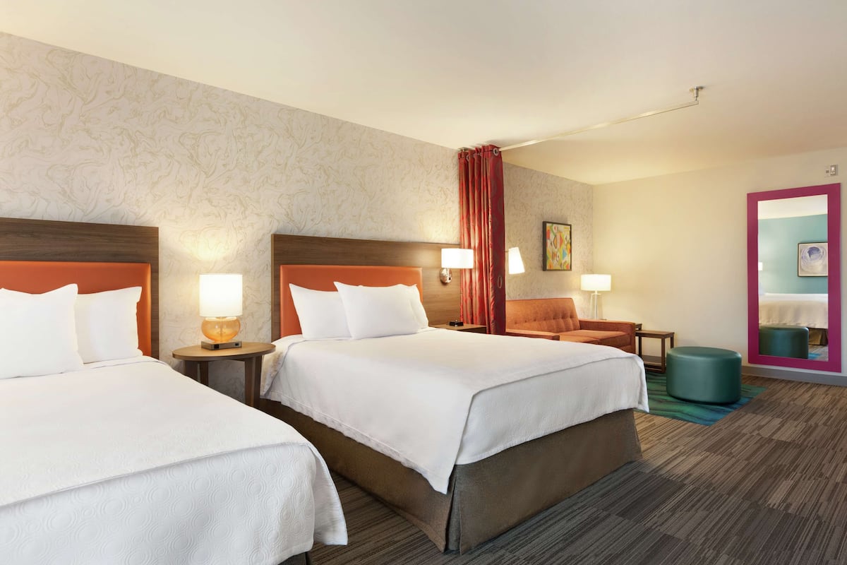 Habitación de hotel con dos camas, una zona de estar y un baño con espejo.