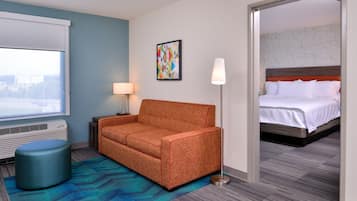 A hotel room with a sofa, a lamp, a painting, and a bed.