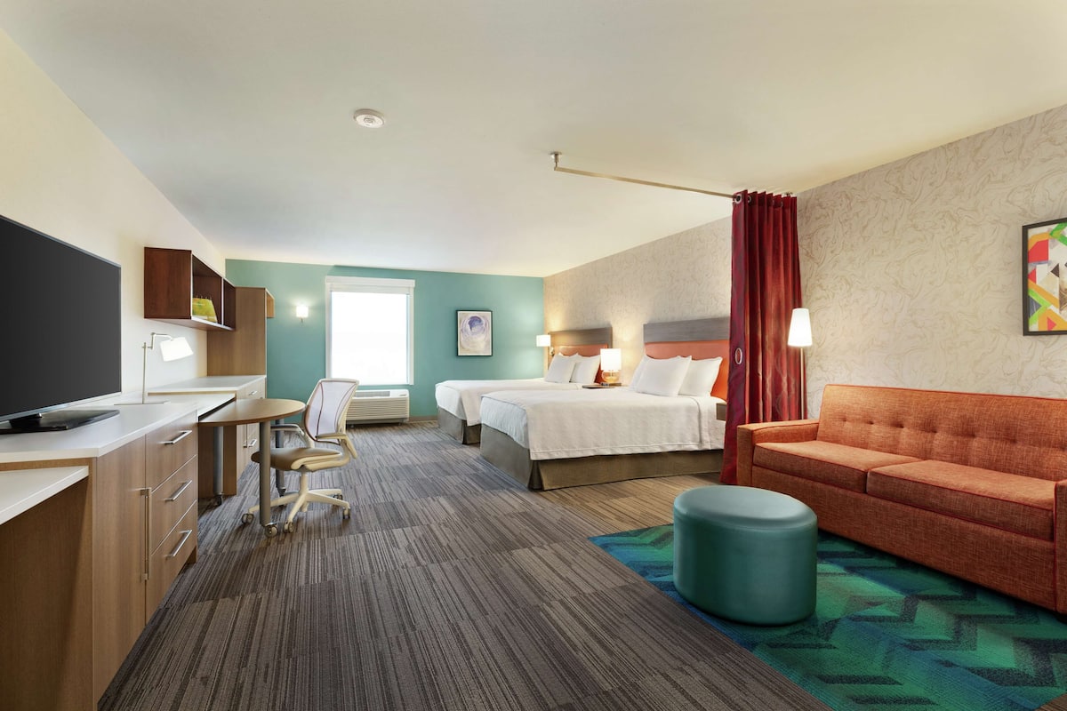 Habitación de hotel con cama, sofá, escritorio con computadora, silla y televisor.