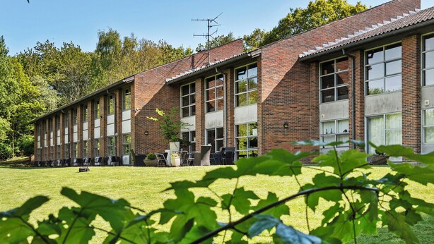 Un long bâtiment en briques, doté de grandes fenêtres et d’une cour verdoyante.