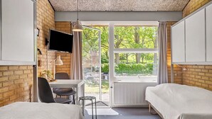 Une chambre d’hôtel avec deux lits, un bureau, une chaise, une télévision et une fenêtre donnant sur un espace verdoyant.