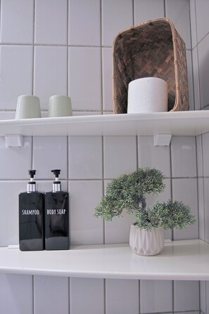 A bathroom shelf with toiletries, a woven basket, and a small potted plant. - Flinten Horsens (Horsens)