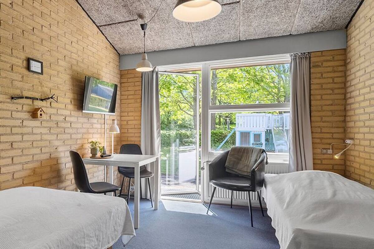 A room with two beds, a table, chairs, a TV, and a window with a view of greenery.