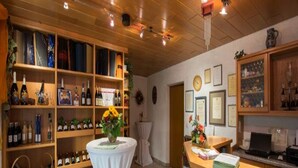 A cozy room with wooden shelves filled with wine bottles, a small round table with a vase, and a wooden counter with a computer. - Weinpension Haberkern (Erlenbach)