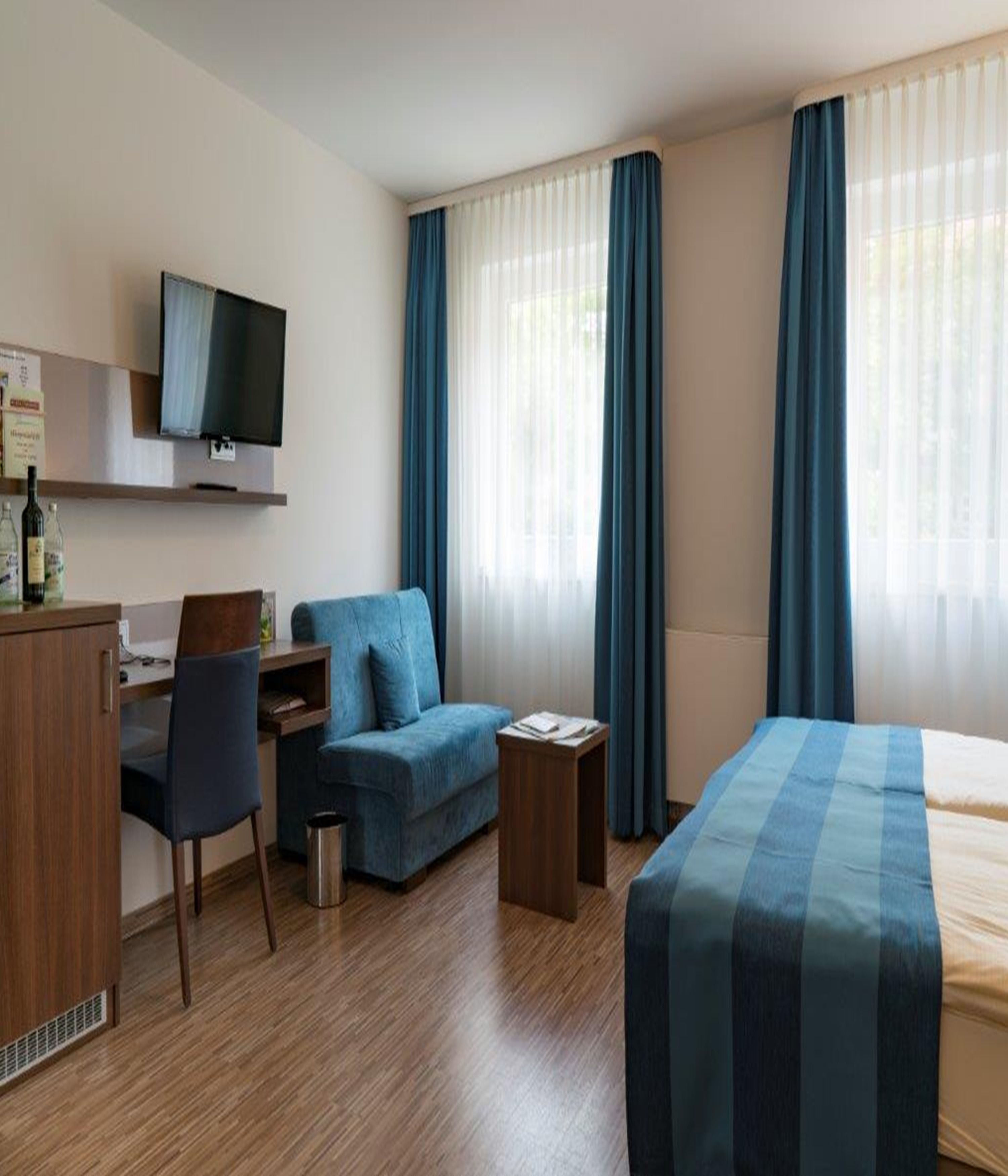 A hotel room with a bed, a desk with a chair, a sofa, and a TV on the wall.