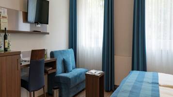A hotel room with a bed, a desk with a chair, a sofa, and a TV on the wall.