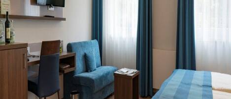 Una habitación de hotel con una cama, un escritorio con silla, un sofá y un televisor en la pared.