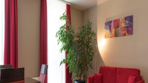 A modern living room with a red sofa, a dining table with red chairs, a potted plant, and a colorful painting on the wall. - Weinpension Haberkern (Erlenbach)