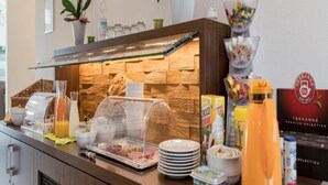 A buffet counter with a variety of food items, including cereal boxes, a juice dispenser, and a coffee machine. - Weinpension Haberkern (Erlenbach)
