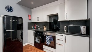 Una cocina moderna con armarios blancos, un refrigerador negro, un microondas, una lavadora y un reloj en la pared.
