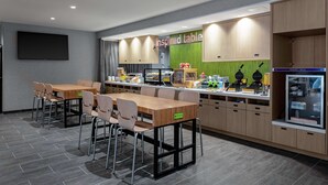 A modern kitchen area with a long counter, multiple seating arrangements, and a refrigerator stocked with dairy products. - Home2 Suites by Hilton North Charleston-University Blvd (North Charleston)