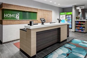 A hotel reception desk with a digital kiosk, a minibar, and a beverage fridge.