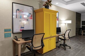 A modern office space with a wooden desk, two office chairs, a yellow filing cabinet, and a framed abstract artwork on the wall.
