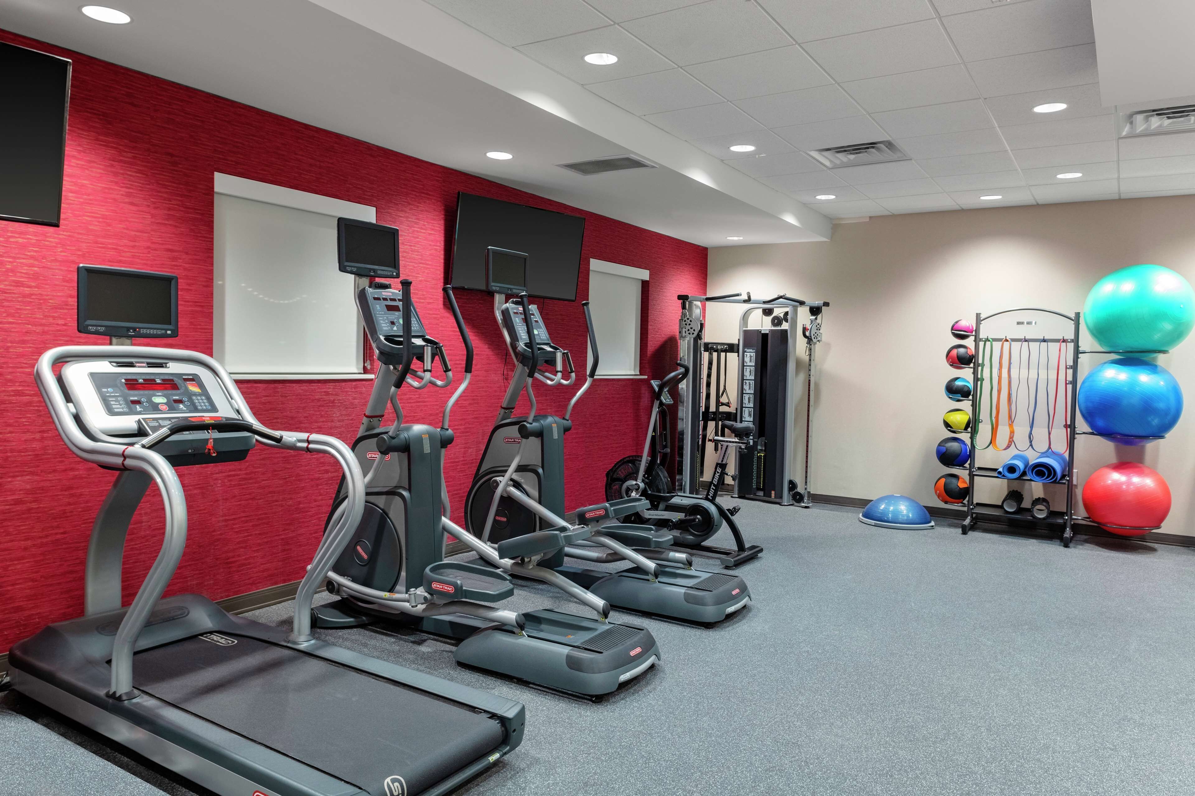 Une salle de sport équipée de tapis de course, de vélos elliptiques et d’une machine de musculation.