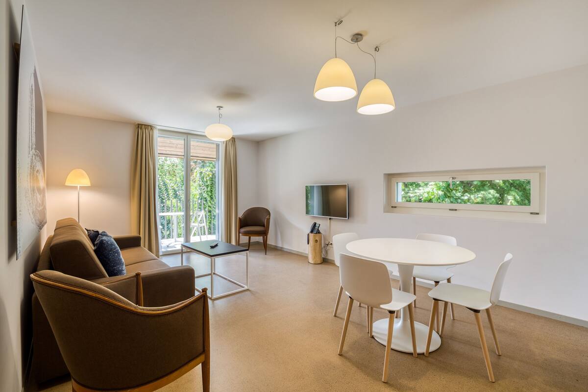A modern living room with a sofa, chairs, a dining table, and pendant lights.