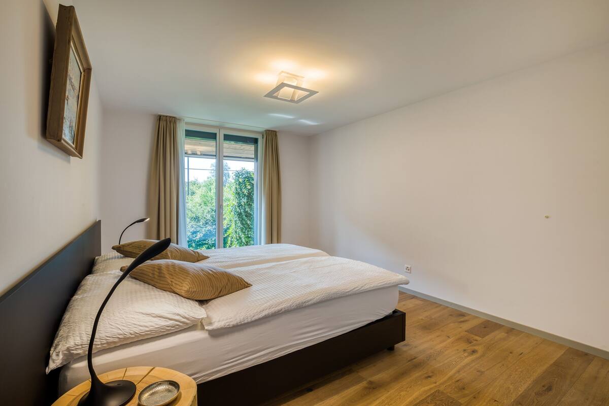 A bedroom with a bed, a bedside lamp, a window with curtains, and a ceiling light fixture.
