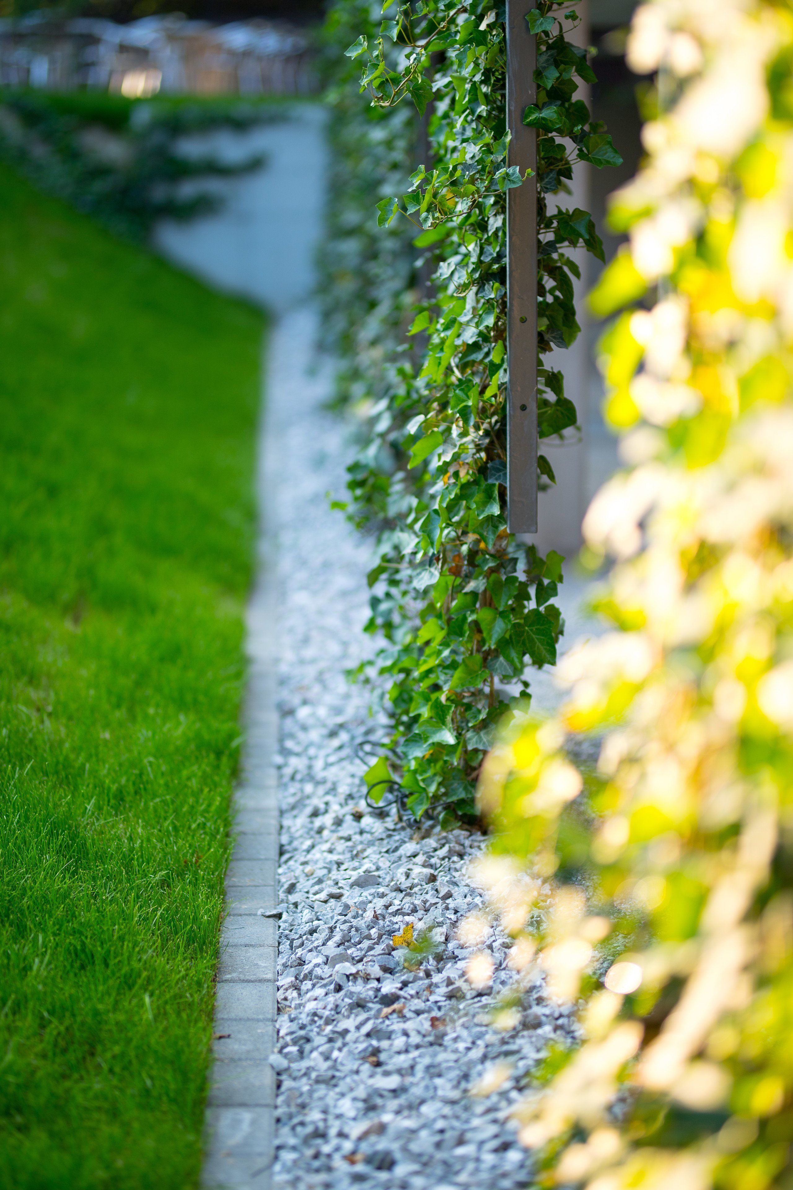 A pathway bordered by a gravel strip and a grassy area, with a metal fence on one side and a wall on the other.