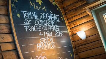 Un menú en pizarra dentro de un espacio de madera, que enumera productos como 'Tomme de chèvre de Botterens' y 'pain & fr'.