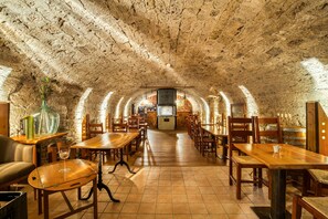 An underground dining area with stone walls, wooden tables, and chairs. - Hôtel-Résidence La Croix-Blanche (Hauterive)