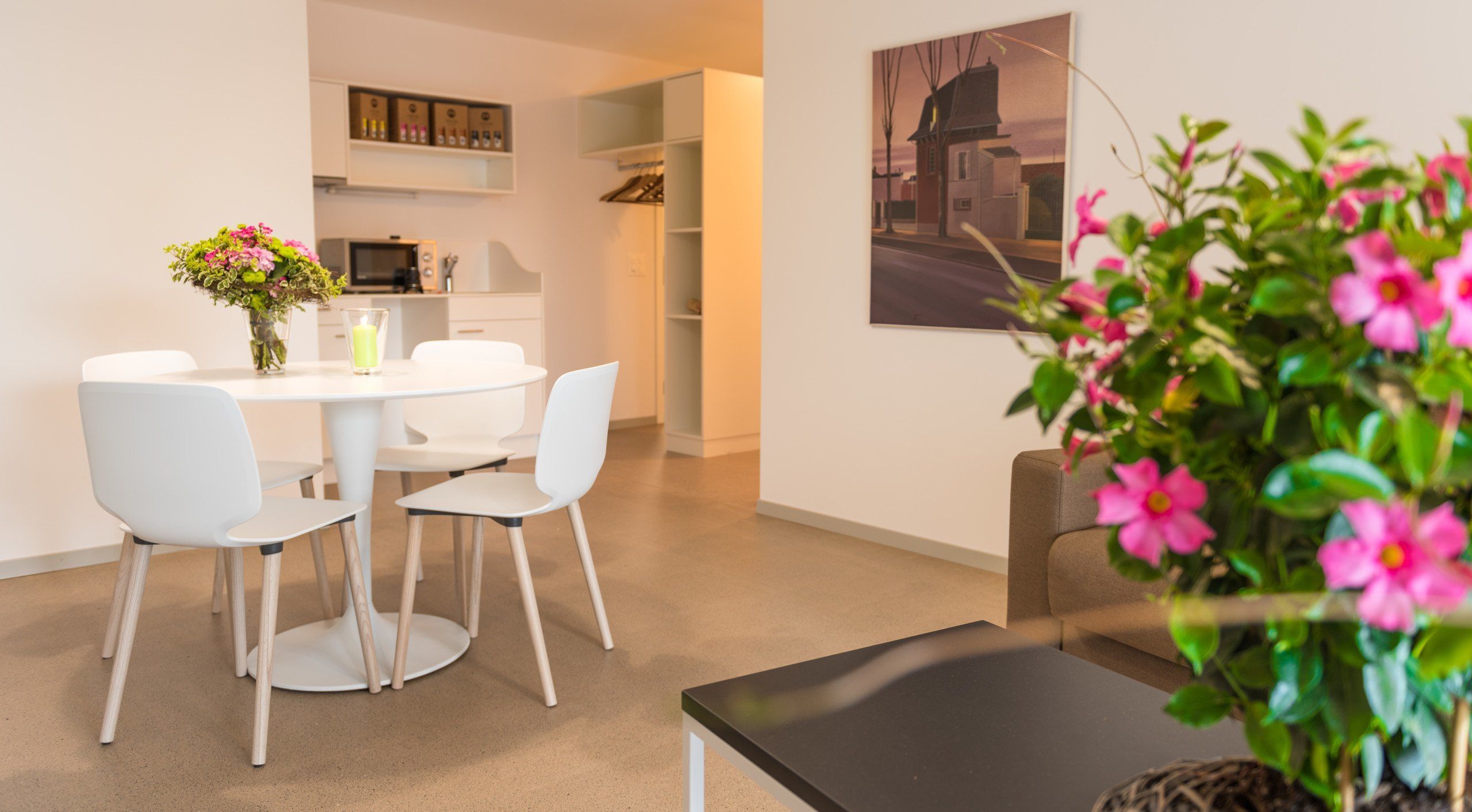 Un espace repas moderne avec une table ronde, des chaises blanches et un vase de fleurs.