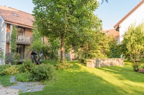 A courtyard with a stone bench, a tree, and a building with a balcony. - Hôtel-Résidence La Croix-Blanche (Hauterive)