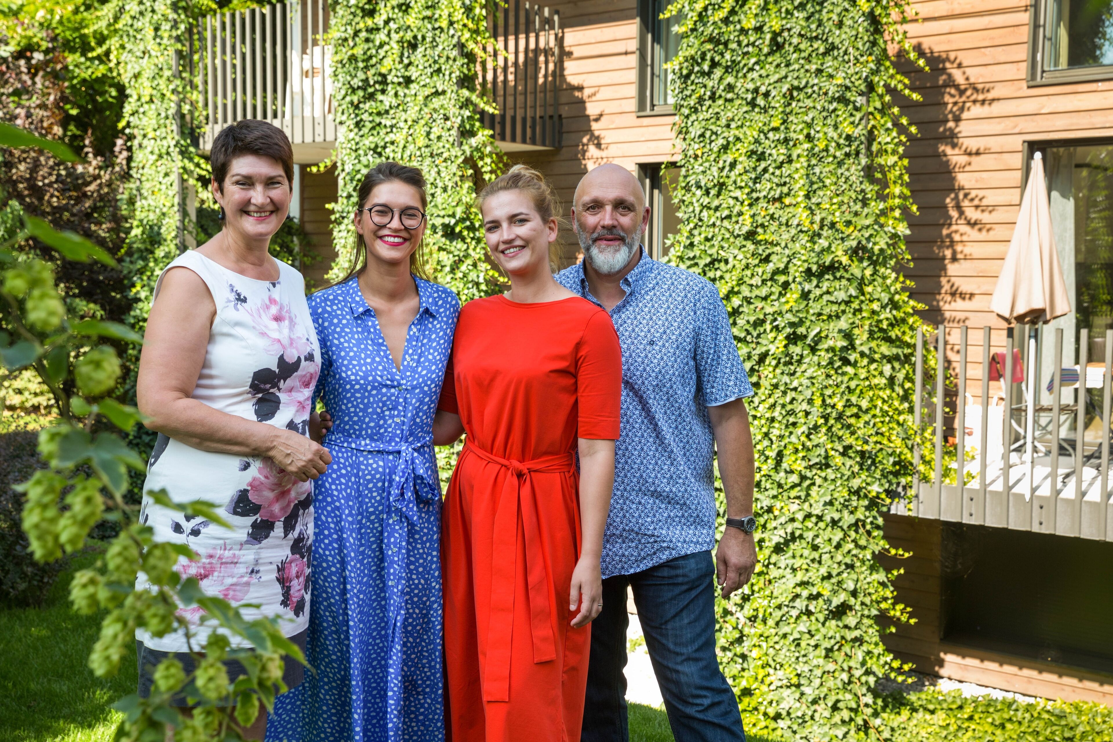 A group of four people standing in a garden with a wooden house in the background.