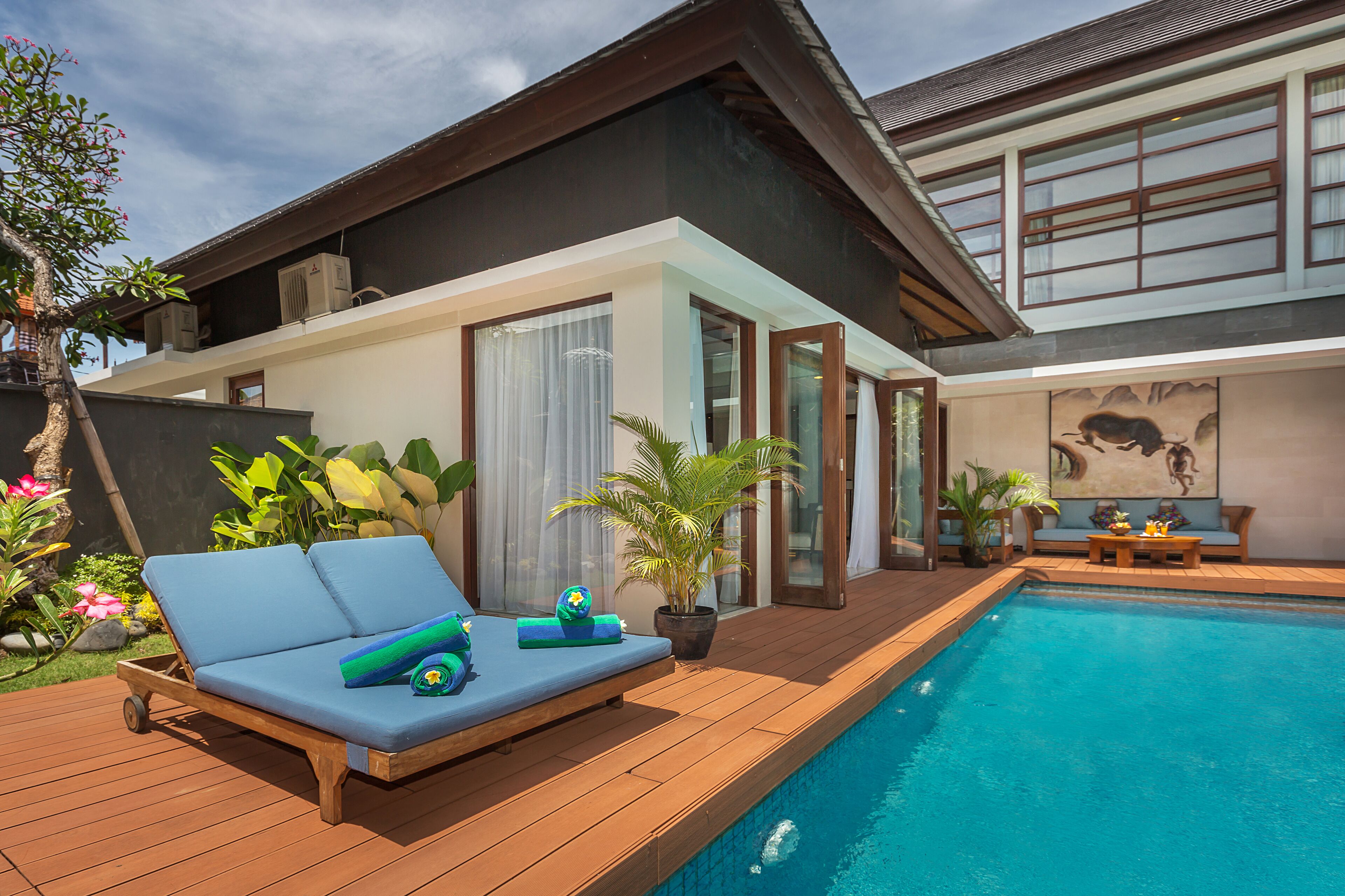 A modern house with a swimming pool, a lounge area with a blue sofa, and a dining set.